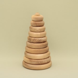 May include: A wooden stacking toy with nine rings of varying sizes, all made of natural wood. The rings are stacked on a cone-shaped base, creating a tower.