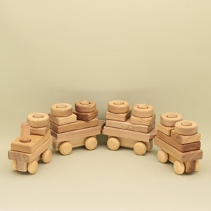 Könnte beinhalten: Ein hölzerner Spielzeugzug mit vier Waggons, die jeweils aus gestapelten Holzklötzen bestehen. Der Zug ist aus Naturholz gefertigt und hat ein schlichtes, klassisches Design.