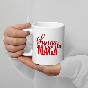 Può includere: Una tazza da caffè in ceramica bianca con una grafica rossa che dice "Chinga tu MAGA".
