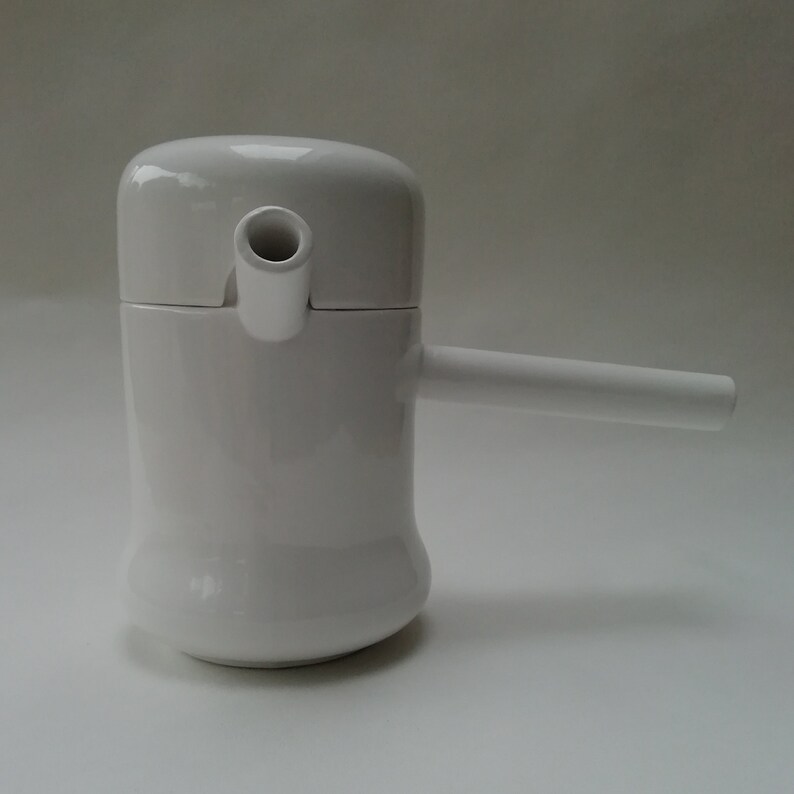 May include: White ceramic teapot with a spout and a handle. The teapot has a rounded body and a lid with a small opening for pouring.