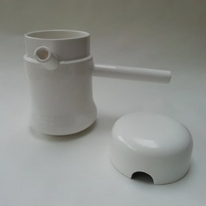 May include: White ceramic coffee pot with a handle and a separate lid. The pot has a unique design with a spout on the side.