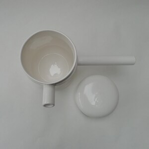 May include: White ceramic teapot with a handle and a separate lid. The teapot has a round body and a spout.