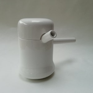May include: White ceramic teapot with a spout and a lid. The teapot has a unique design with a curved body and a rounded lid.