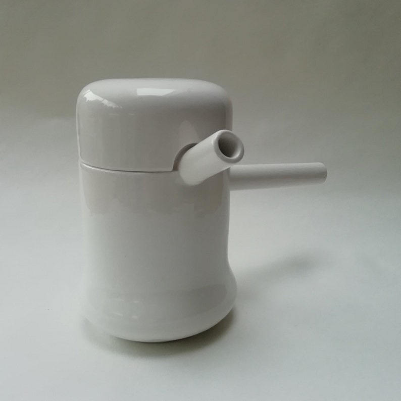 May include: White ceramic teapot with a spout and a lid. The teapot has a unique design with a curved body and a rounded lid.