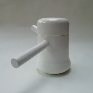 May include: White ceramic teapot with a rounded body and a spout on the side. The teapot has a handle that extends out from the side.