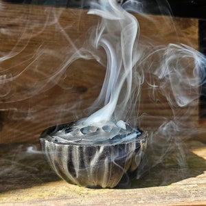 May include: A black metal incense burner with a decorative design, releasing wispy white smoke.