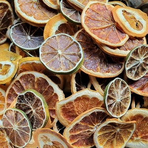 May include: A close-up of a variety of dried citrus fruit slices, including orange, lime, and grapefruit. The slices are arranged in a random pattern and are a mix of light and dark brown colors.