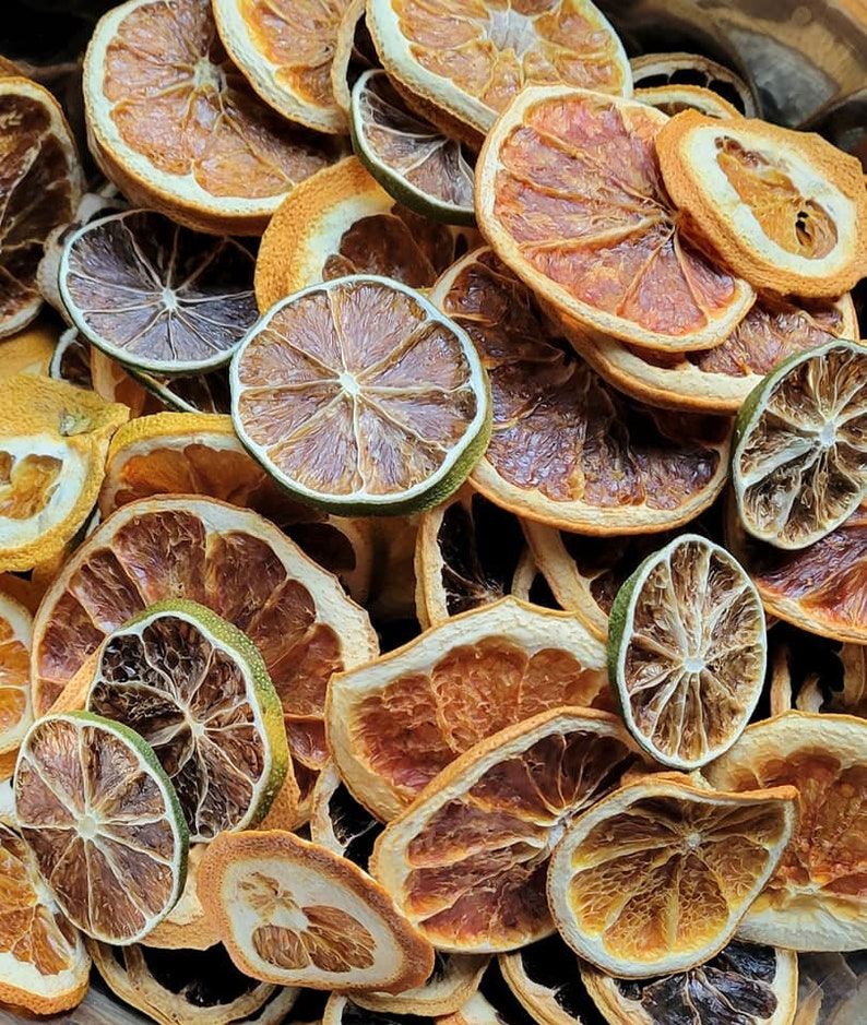 May include: A close-up of a variety of dried citrus fruit slices, including orange, lime, and grapefruit. The slices are arranged in a random pattern and are a mix of light and dark brown colors.