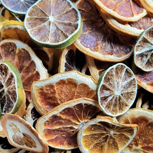 May include: A close-up of a variety of dried citrus fruit slices, including orange, lime, and grapefruit. The slices are arranged in a random pattern and are all different sizes and shapes. The colors of the fruit are vibrant and range from bright orange to deep yellow to green.