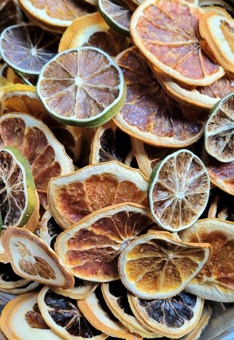 May include: A close-up of a variety of dried citrus fruit slices, including orange, lime, and grapefruit. The slices are arranged in a random pattern and are all different sizes and shapes. The colors of the fruit are vibrant and range from bright orange to deep yellow to green.