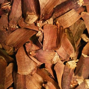 Puede incluir: Primer plano de un montón de escamas de piña secas, de color marrón rojizo. Las escamas tienen una superficie texturizada y varían en tamaño y forma. La iluminación crea sombras, añadiendo profundidad a la composición.