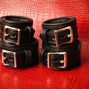 May include: Four black leather cuffs with silver buckles. The cuffs are stacked in pairs.