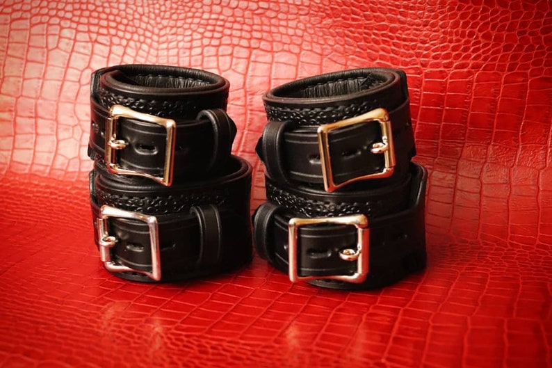 May include: Four black leather cuffs with silver buckles. The cuffs are stacked in pairs.