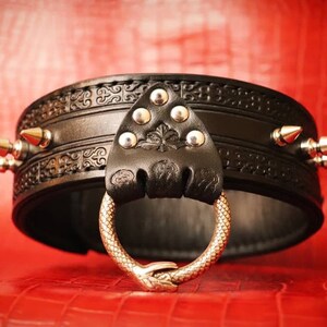 May include: Black leather collar with silver studs and a snake-shaped metal ring. The collar has an intricate embossed design.
