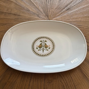 May include: White oval serving platter with a decorative bird and tree design in the center. The birds are orange and green, set against a beige and green circular border. A thin green line borders the edge of the platter.