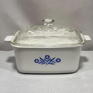 May include: White rectangular casserole dish with a clear glass lid and a clear glass knob. The dish has a blue floral design on the front. The dish has white handles on each side.