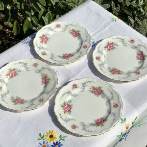 Puede incluir: Cuatro platos de cerámica blanca con un diseño floral. Los platos tienen un borde festoneado y un borde dorado. Las flores son rosas, azules y verdes.