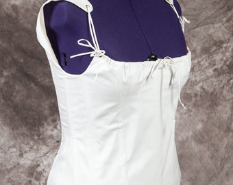 May include: White cotton corset with adjustable straps and a lace-up front. The corset is displayed on a purple mannequin.