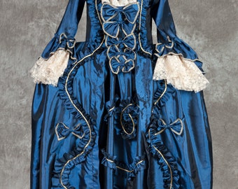 May include: A blue and gold brocade gown with a lace trim and a fitted bodice. The gown has a full skirt and is decorated with bows and ruffles.