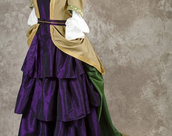 May include: A historical-style dress on a mannequin. The dress features a layered purple skirt, a tan bodice with gold trim, and white sleeves. A green train extends from the back of the dress.