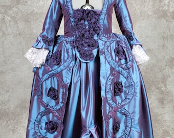 May include: A blue and purple silk dress with a fitted bodice and a full skirt. The dress has a decorative trim of purple rosettes and a lace trim on the sleeves.