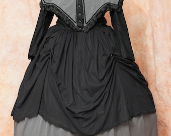 May include: A black and gray Victorian-style dress with a cape. The dress has a black skirt with a gray underskirt and a gray cape with black trim.