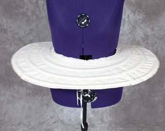 May include: A white, circular, fabric hoop skirt with multiple layers and a ruffled edge. The hoop skirt is displayed on a purple dress form.