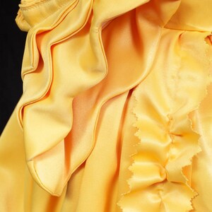 以下が含まれることがあります： 袖とスカートにフリルが付いた黄色のサテンのドレスです。