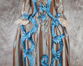 May include: A brown and teal formal gown with a fitted bodice and a full skirt. The gown is decorated with teal ruffles and bows.