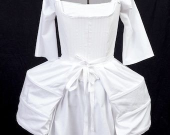 May include: A white cotton underskirt with a gathered skirt and a fitted bodice. The skirt has two large pockets on each side. The bodice has a square neckline and a tie at the waist.