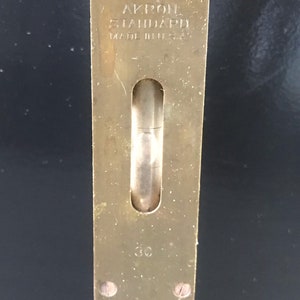 May include: A brass level with a wooden handle. The level has a glass vial and is labeled "AKRON STANDARD MADE IN U.S.A."