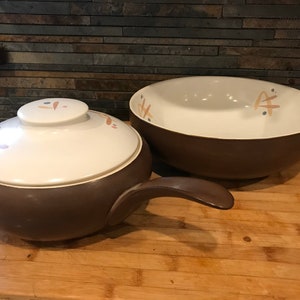May include: A brown ceramic casserole dish with a lid and a matching brown bowl. Both pieces have a white interior with a light brown and orange floral design.