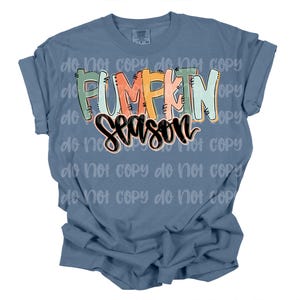 Peut inclure: Un t-shirt bleu avec l'inscription "PUMPKIN SEASON" dans une typographie color&eacute;e et ludique. Le texte est en orange, vert et noir, cr&eacute;ant un th&egrave;me automnal festif. Le t-shirt a des manches courtes et une coupe d&eacute;contract&eacute;e.