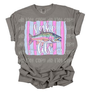 May include: A gray t-shirt with a pink and blue striped design featuring a rainbow trout and the text "lake life".