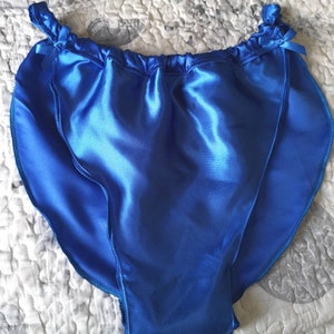 May include: Royal blue satin underwear with a gathered waistband and small bow details. The shiny fabric reflects light, highlighting the smooth texture and tailored seams. A classic lingerie piece.