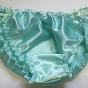May include: Light blue satin underwear with ruffled edges and small bows. The delicate garment has a smooth, shiny texture and a comfortable design. A feminine piece of lingerie.