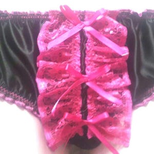 May include: Black satin underwear with a pink lace front and pink ribbon accents. The edges are trimmed with a scalloped pink lace. The center features a vertical design with pink bows.