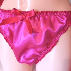 May include: Bright pink satin underwear with red ribbon ties and bows. The edges are trimmed with delicate red lace. The satin fabric has a shiny, smooth texture.