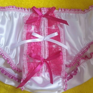 May include: White satin underwear with pink lace and ribbon accents. The underwear features a ruffled trim and decorative bows. The center panel is made of pink lace and is adorned with white and pink ribbons.