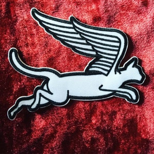 May include: White felt patch of a cat with wings, the cat is running and has a black outline. The wings are black and white and are behind the cat.