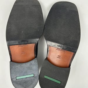 K&ouml;nnte beinhalten: Ein Paar schwarze Lederschuhe, Sohlen nach oben. Die Sohlen sind aus schwarzem Gummi mit einem strukturierten Muster. Die Abs&auml;tze haben einen gr&uuml;nen Streifen und den Aufdruck "SALAMANDER RIDER". Die Innensohlen sind aus braunem Leder.