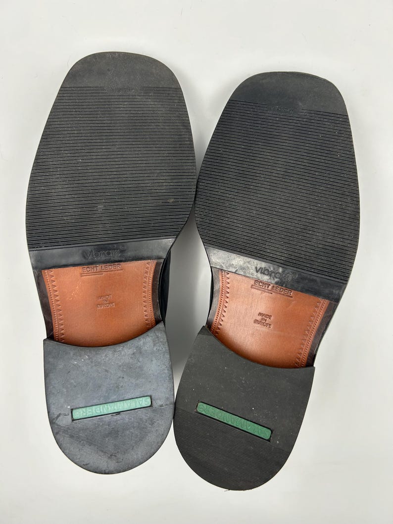 K&ouml;nnte beinhalten: Ein Paar schwarze Lederschuhe, Sohlen nach oben. Die Sohlen sind aus schwarzem Gummi mit einem strukturierten Muster. Die Abs&auml;tze haben einen gr&uuml;nen Streifen und den Aufdruck "SALAMANDER RIDER". Die Innensohlen sind aus braunem Leder.