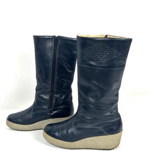 May include: A pair of navy blue tall boots with a side zipper and a beige sole. The boots have a diamond-shaped pattern near the top and are made of a smooth, possibly leather, material.