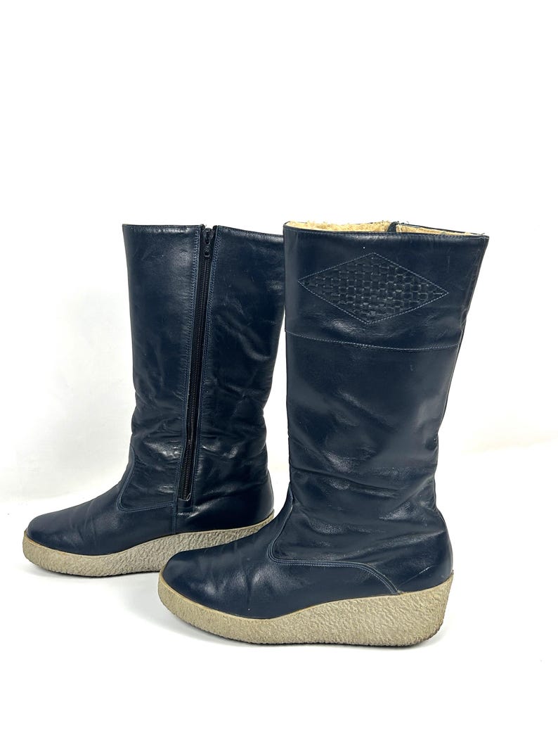 May include: A pair of navy blue tall boots with a side zipper and a beige sole. The boots have a diamond-shaped pattern near the top and are made of a smooth, possibly leather, material.