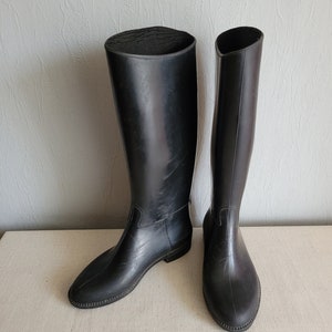 Puede incluir: Un par de botas de montar de goma negra con un eje alto y un tacón bajo.