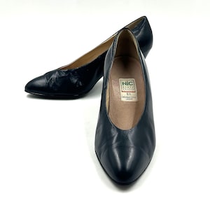 Può includere: Un paio di décolleté in pelle blu navy con punta e tacco basso. Le scarpe hanno un design classico e sono su sfondo bianco. L'interno di una scarpa mostra un'etichetta.