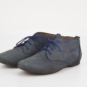 May include: A pair of blue suede ankle boots with blue laces. The boots have a rounded toe and a low heel. The shoes are displayed on a white background. The boots are a casual style.