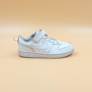 以下が含まれることがあります： ベルクロストラップとナイキのスウッシュロゴが付いた白い革のスニーカー