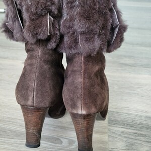 May include: A pair of brown suede boots with faux fur trim around the top of the boot. The boots have a high heel.