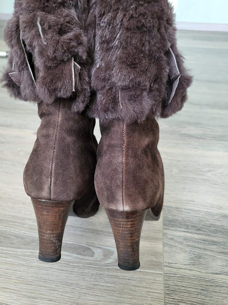 May include: A pair of brown suede boots with faux fur trim around the top of the boot. The boots have a high heel.